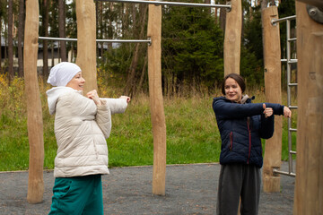 Cancer survivor and instructor doing warm-up stretches on sports ground, concept of support, motivation, and physical therapy.