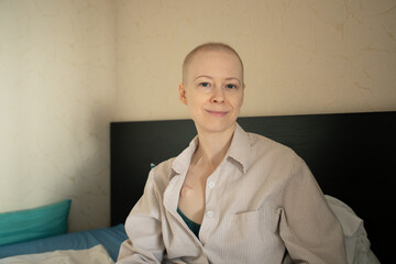 Young female cancer patient waking up in bed, natural warm light in bedroom, bald head and delicate features, concept of life after chemotherapy, home recovery, oncology awareness
