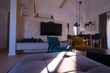 Obraz premium Modern open-plan living and dining area with an integrated kitchen, featuring a comfortable sofa, stylish armchairs, and a bar-height dining table. Wooden floors and ceiling beams enhance this