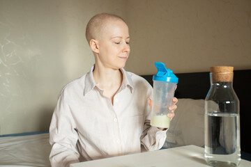 Young cancer patient hydrating with protein shake by bedside, woman with alopecia from chemotherapy using nutritional supplement for strength and energy,