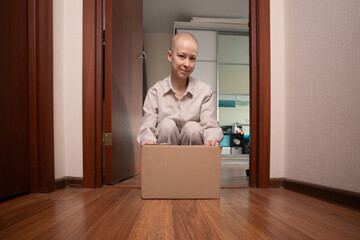 Oncology patient in striped pajamas kneeling in doorway with shipping box, safe home delivery of prescriptions and medical nutrition, staying indoors during weakened immunity and treatment.