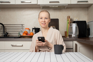 cancer survivor with short regrown hair sits in cozy home kitchen, holding a black mug of tea and gently smiling, concept of remission, hope, self care, slow morning ritual and healthy daily routine