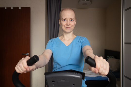 Cancer patient works out at home on an exercise bike, woman after chemotherapy training in bedroom, indoor cardio workout for oncology rehabilitation, home fitness and recovery