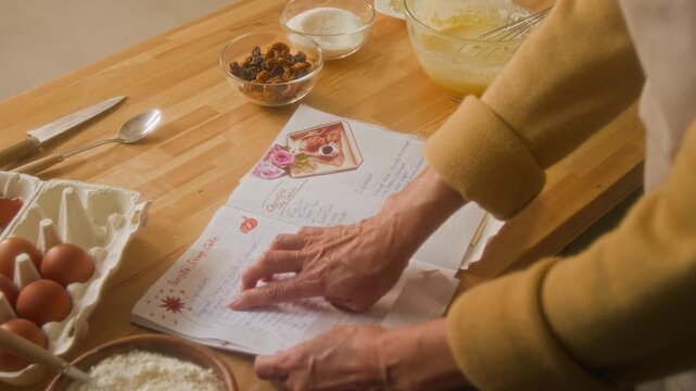 Cropped shot of hands of unrecognizable housewife using cookbook at kitchen counter with ingredients for home cooking