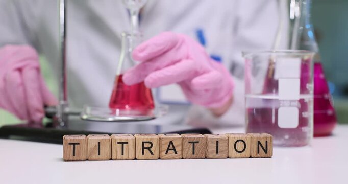 Lab worker in protective gloves carefully adjusts burette valve during titration. Wooden cubes arranged to form word Titration on laboratory table