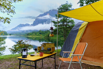Camping tents at morning, vintage cabin tents, antique oil lamps, retro chairs, and a group of camping tents with outdoor coffee-making facilities on wooden tables in a forest camping area.