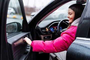 Young woman driver smiling, opening car door on a rainy day trip
