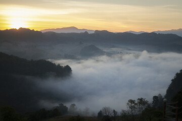 Serene golden sunrise over mountain landscape with valley filled with fog and mist. Tranquil nature scenery offers peaceful and majestic outdoor view from above