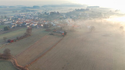 Foggy Bavarian landscape during morning sunrise phase with forest background and small village close which is called P&ouml;rnbach and is located at the region of Pfaffenhofen