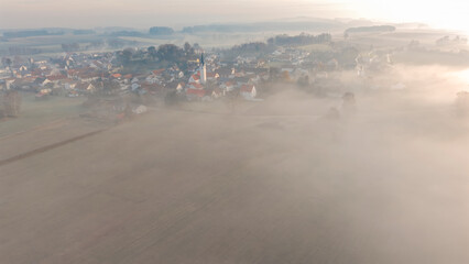 Foggy Bavarian landscape during morning sunrise phase with forest background and small village close which is called P&ouml;rnbach and is located at the region of Pfaffenhofen
