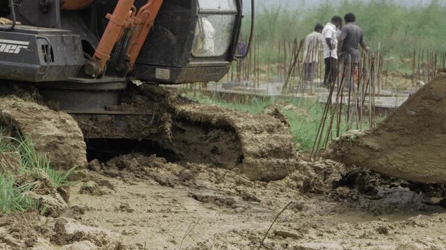 Action-packed JCB Crane Digging in Muddy Ground with Workers in the Background