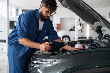 Obraz premium Checking the information. Auto service specialist examining vehicle condition