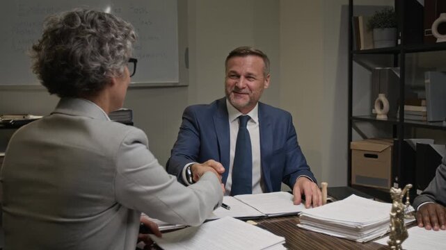 Medium pan shot of smiling senior Caucasian male partner at legal firm thanking female lawyer for good work and valuable contribution during case review at team meeting, while preparing for trial