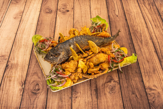 Freshly fried seafood jalea, presented colorfully with whole prawns, calamari rings, and scallops, garnished with lemon wedges and lettuce leaves