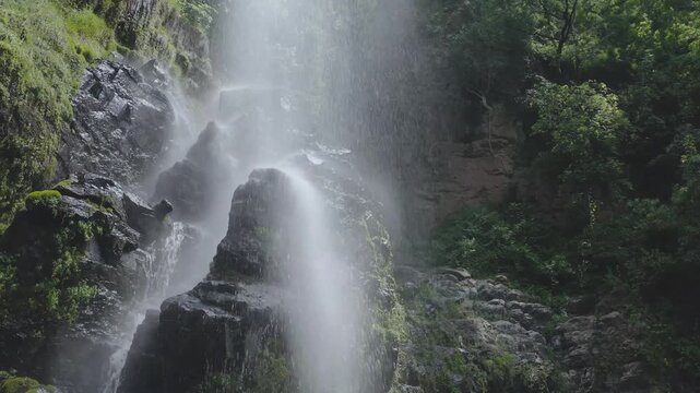 Water cascades down a rocky waterfall surrounded by lush greenery and trees.