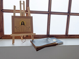 Religious illustration of Jesus on easel beside old psalter and bible near window