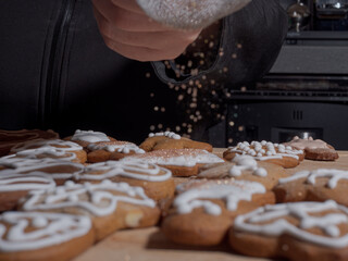 A hand sprinkles sugar over Christmas gingerbread cookies on a wooden board in the kitchen.