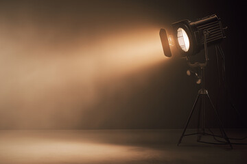 Cinematic studio spotlight shining through haze in dark room, warm beam of light with dramatic shadows and empty copy space, stage lighting equipment on tripod, moody theater background for banner