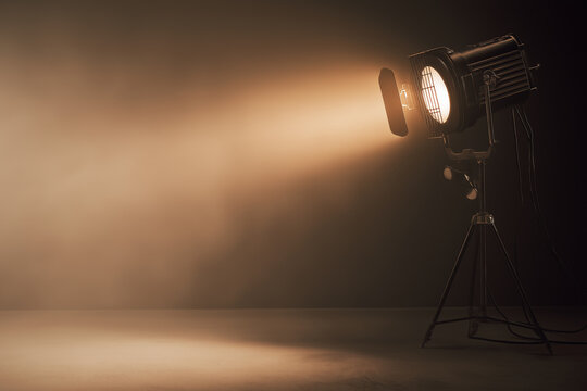 Cinematic studio spotlight shining through haze in dark room, warm beam of light with dramatic shadows and empty copy space, stage lighting equipment on tripod, moody theater background for banner