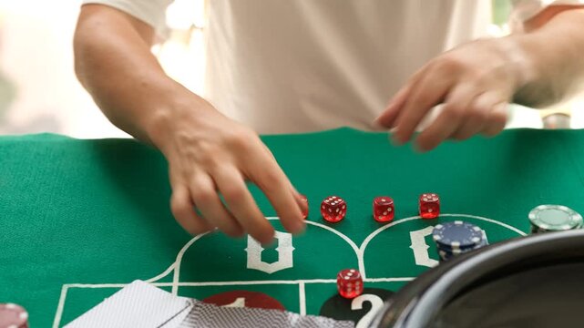 Male hands move dice throwing near chips on green gambling table layout. Casino player places small bet while rolling red dice during game in casino