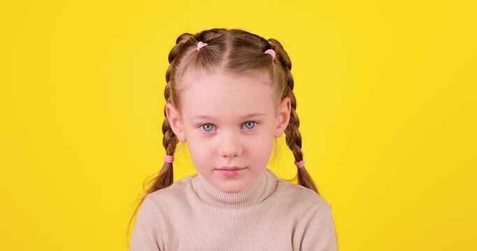 4K video of a serious child gradually beginning to smile on a bright yellow background. Emotional transition from neutral to happy expression, positivity and mood change concept with clean studio comp