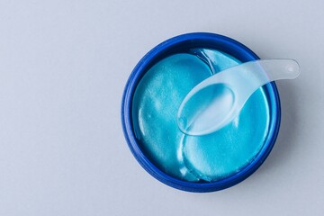 Eye patches. Hydrating Blue Gel Face Mask with Applicator Spoon in a Blue Container on a Light Background, top view with copy space