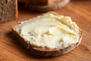 Slice of artisanal rye bread spread with butter on wooden background, closeup view