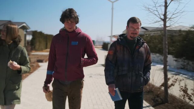 three white adults walking suburban boardwalk, friendly discussion with coffee and papers, community planning vibe and outreach energy, casual jackets, spring sunlight, engaged neighbors sharing ideas