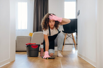 Tired, taking a break. Busy woman cleaning the floor on her knees with a bucket and cloth during household chores