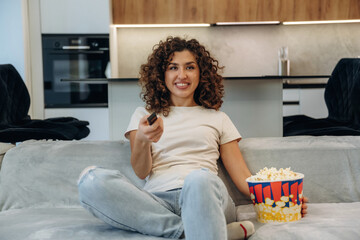 Weekend activities. Happy woman relaxing on a sofa with popcorn, watching TV and enjoying her leisure time at home