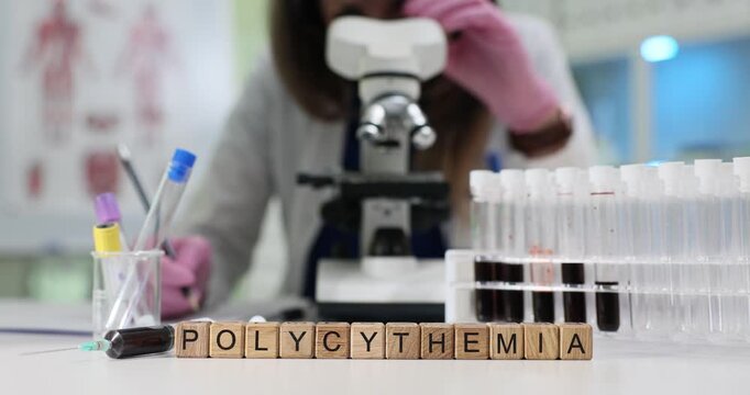 Woman in lab coat adjusts focus of microscope to examine blood sample. Wooden blocks arranged on table form medical term Polycythemia by test tubes
