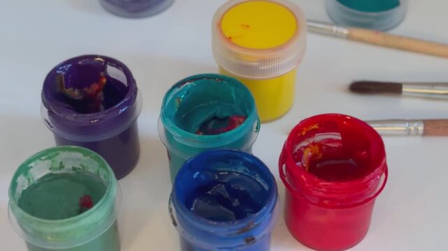 A set of gouache paints in jars, vibrant colors, close-up. Brushes and paints on a table. Art, hobby, school