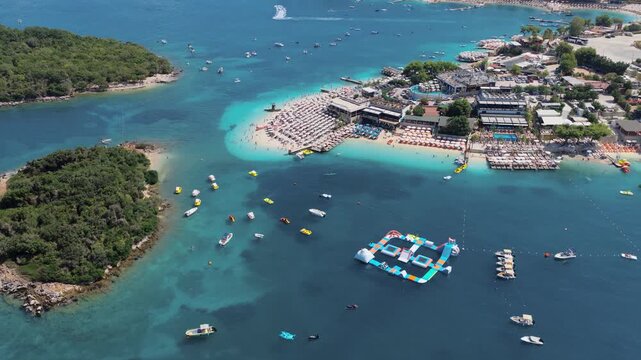 Aerial view of the vibrant Ksamil beach where turquoise waters meet the sandy shore bustling with beachgoers and boats, Ksamil, Vlore County, Albania.