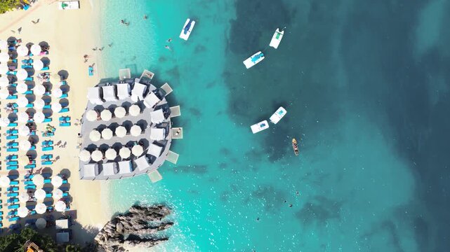 Aerial view of beach umbrellas dotting the sandy shore, contrasted by the turquoise waters with boats, creating a striking summer scene, Ksamil, Vlore County, Albania.