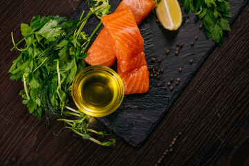 Fresh salmon fillets arranged on a slate board with vibrant green herbs, a slice of lemon, and a...