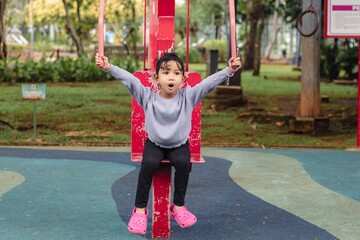 A cute little Indonesian girl trying out a shoulder pull exercise machine in the park