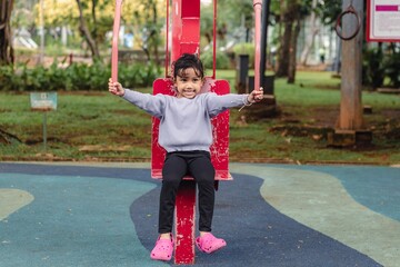 A little Indonesian girl exercising outdoors in the park, trying out a shoulder pull exercise machine