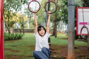 A little Indonesian girl hanging on ring pull up bar outdoors in a city park