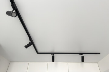 Modern ceiling track lighting system featuring sleek black fixtures illuminating a minimalist interior space with a clean white ceiling and cabinetry enhancing contemporary design aesthetics