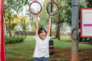 A little Indonesian girl hanging on ring pull-up bar outdoors in a public park