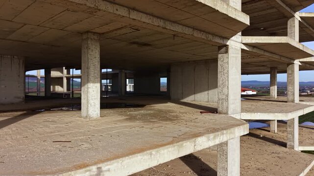 At a construction site, a bare concrete structure rises towards the sky, showcasing levels still under development amidst a peaceful landscape with distant hills.