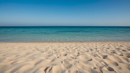 a serene beach scene with clear water under a bright blue sky. Fine, golden sand stretches out towards the calm ocean, creating a sense of peace and tranquility