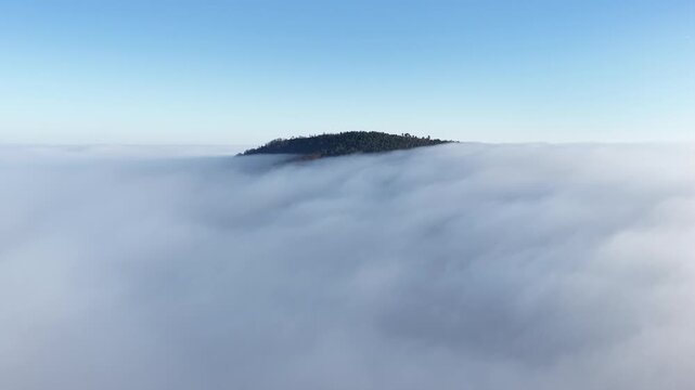 Aerial view of the peak of a mountain piercing through a sea of fluffy white clouds under a clear blue sky, Orschwiller, Grand Est, France.
