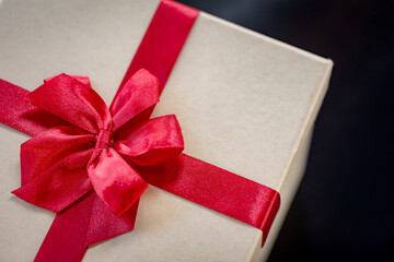 Close-up of Luxurious Red Satin Ribbon and Bow on Beige Gift Box Against Dark Background