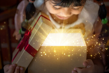 Excited Child Looking into Magical Open Gift Box with Golden Glowing Light and Sparkles from Above
