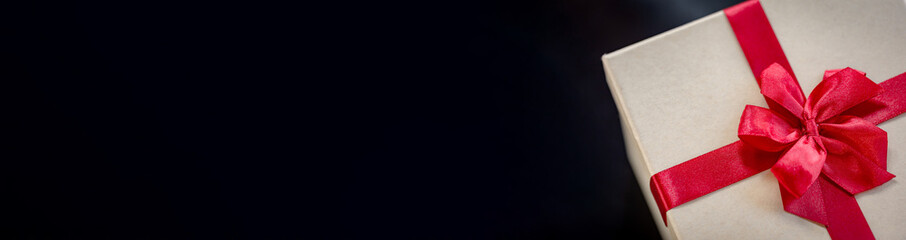 Elegant Gift Box with Bright Red Ribbon on Black Background, Perfect for Christmas, New Year, or Anniversary Banner/Copy Space.