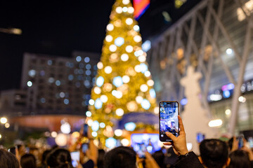 Hand Taking Photo of Illuminated Christmas Tree in City Crowd with Mobile Phone, Festive Atmosphere