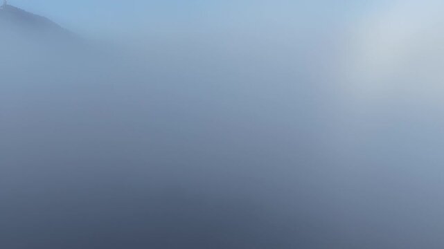 Aerial view of a thick blanket of ethereal fog rolling over the landscape, partially obscuring a distant mountain, Orschwiller, Grand Est, France.
