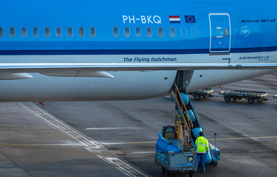 Amsterdam, The Netherlands, 13.12.2025, Airport Ground Handler Loading Luggage onto Baggage Conveyor Belt at Schiphol Airport