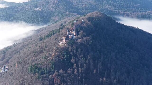 Aerial view of Chateau du Haut-Koenigsbourg, a medieval castle on a hilltop surrounded by lush forests and low-lying clouds, Orschwiller, Grand Est, France.